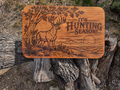 Rustic wood-toned board with deer, tree, mountain landscape and It's Hunting Season design