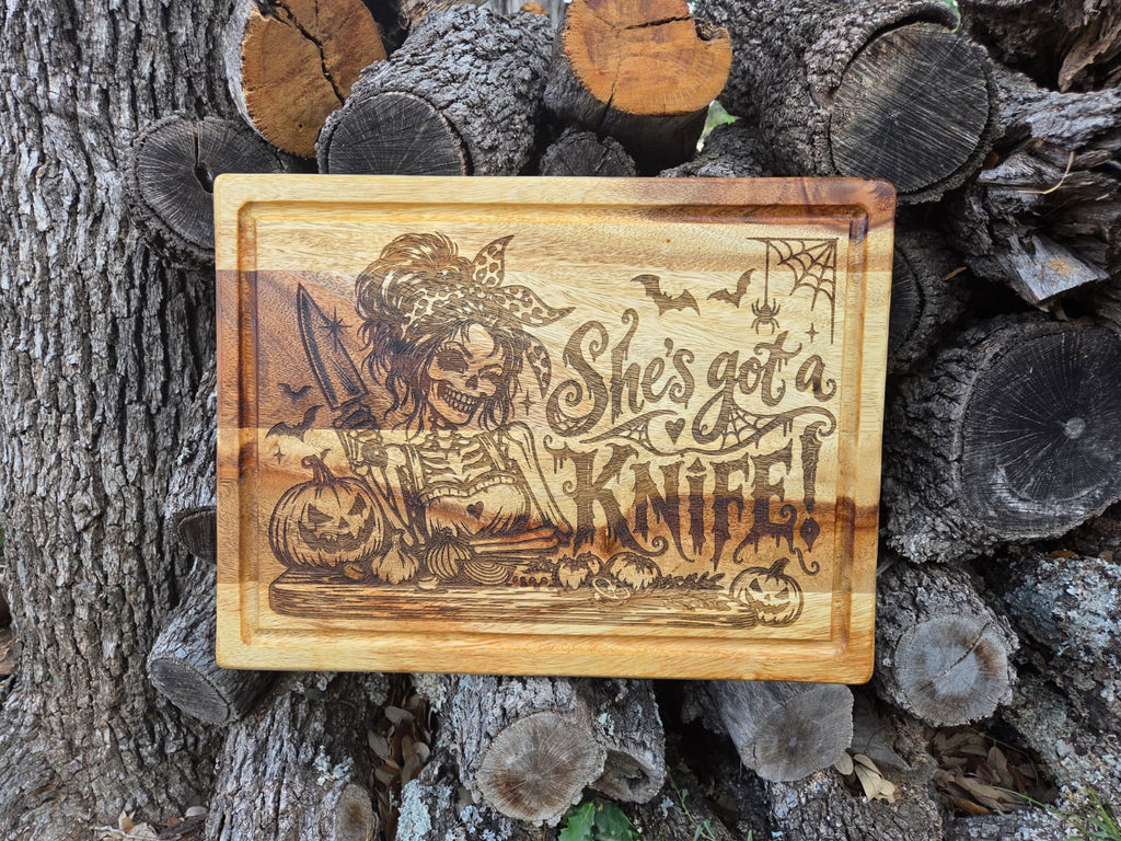 Engraved Halloween cutting board with skeleton holding knife, pumpkins, bats and She's got a knife lettering