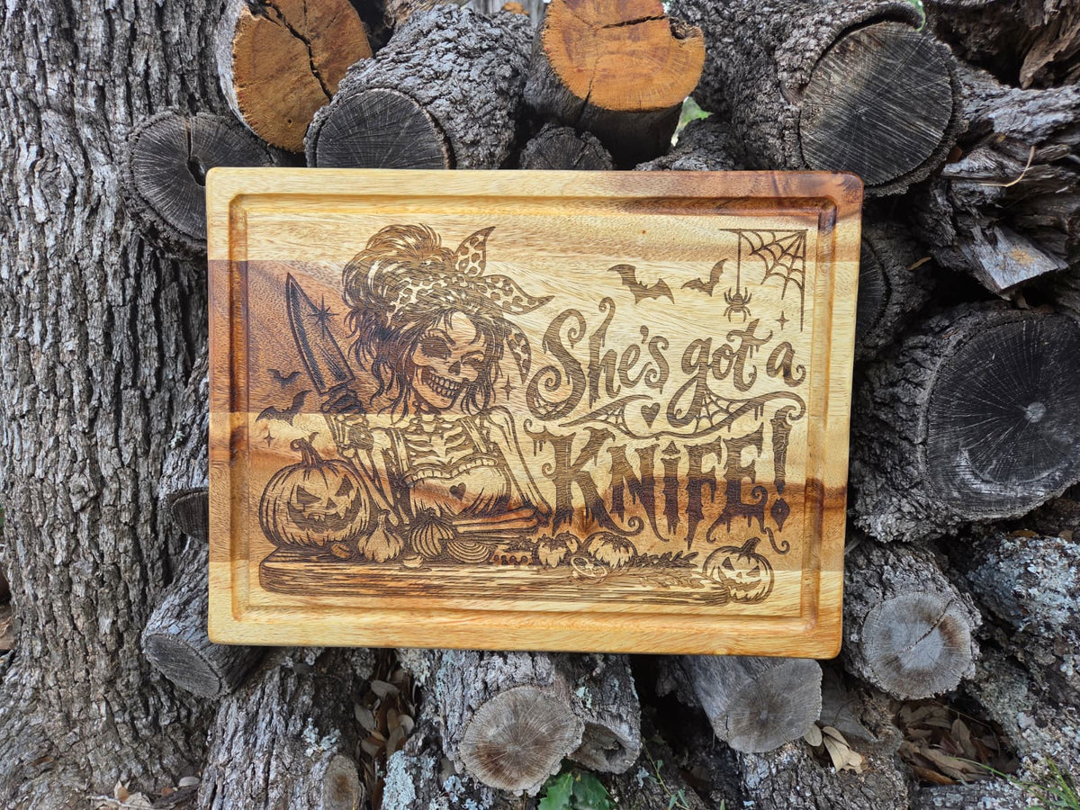 Engraved Halloween cutting board with skeleton holding knife, pumpkins, bats and She's got a knife lettering